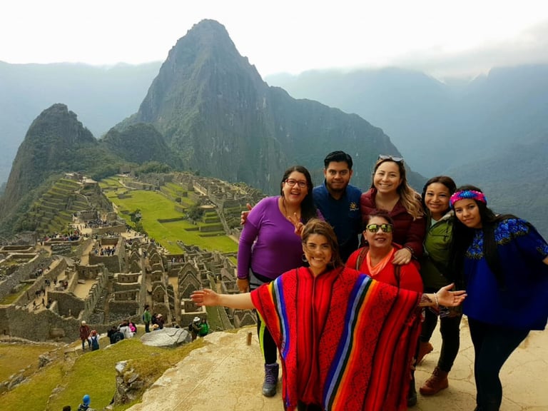 Group of tourists posing at Machu Picchu with mountain peaks and ancient ruins visible in the background